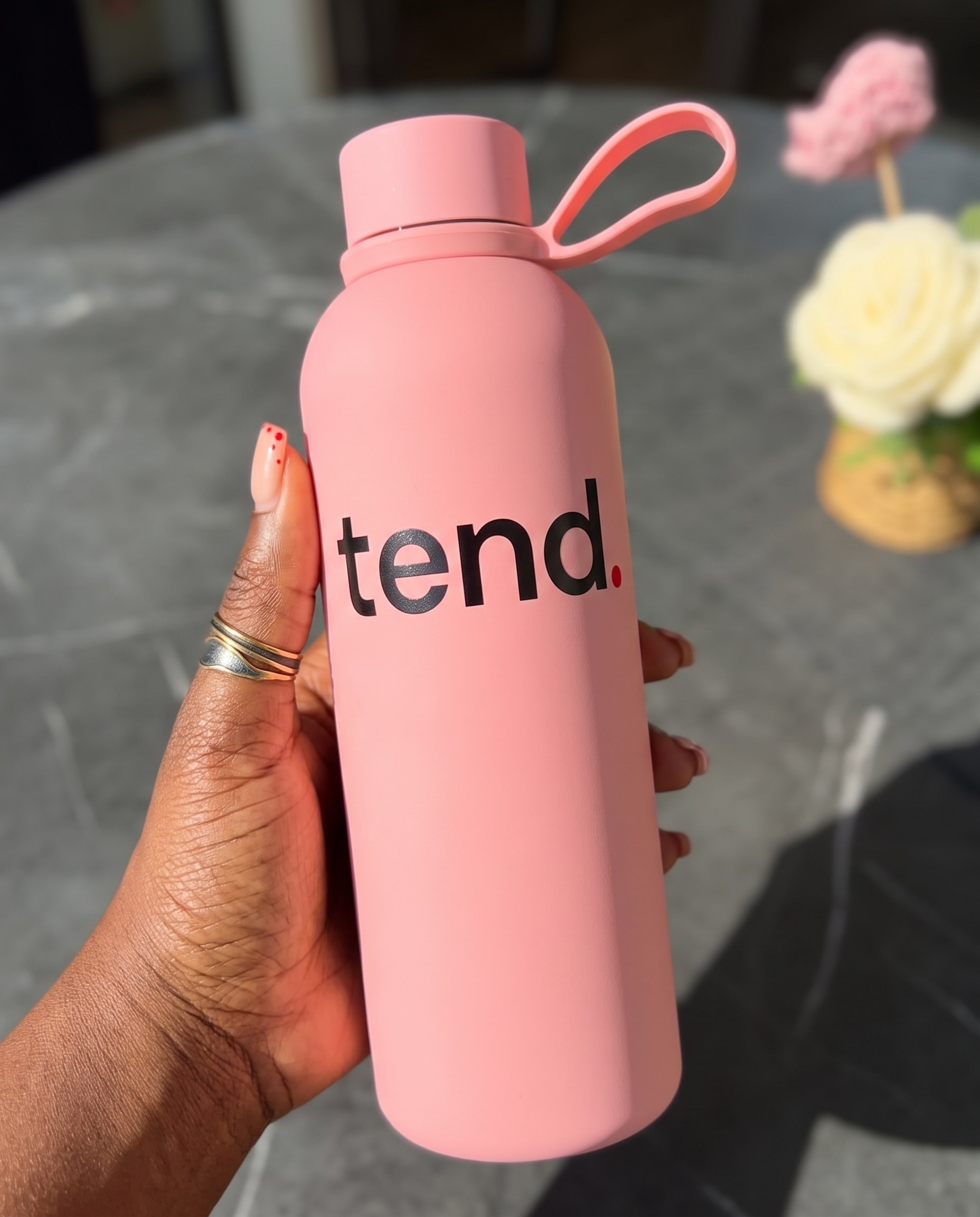 A hand holding the pink tend. water bottle outdoors in the sun